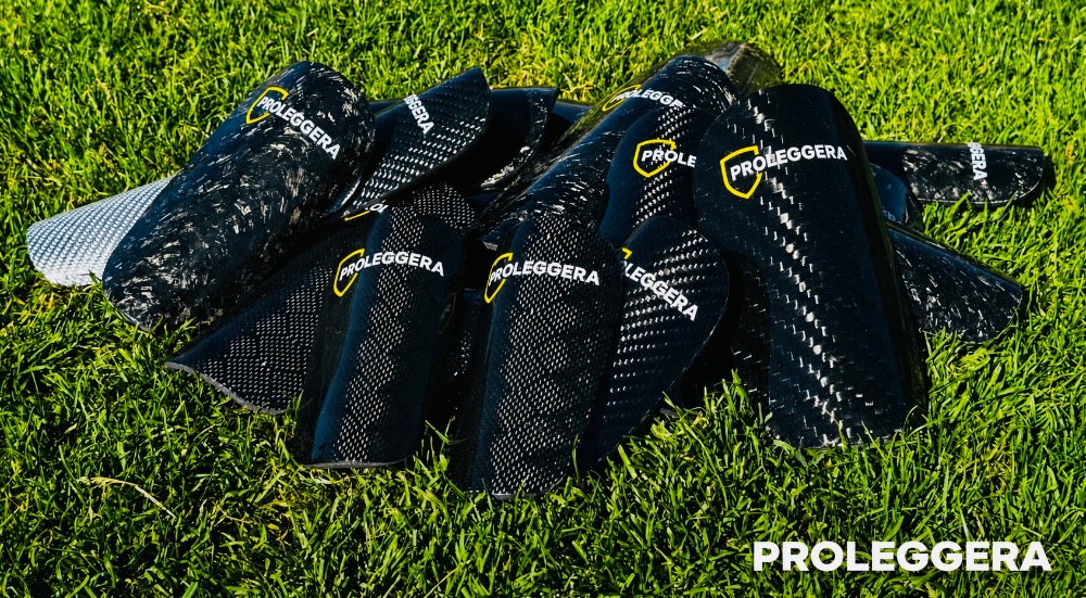 Haufen mehrerer Fußball-Carbon-Schienbeinschoner PROLEGGERA, die auf dem Rasen eines Fußballfeldes liegen.